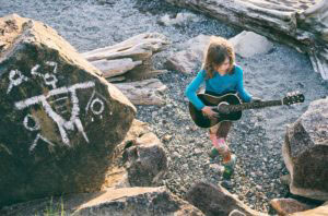 Child playing guitar at Carkeek Park in Seattle by the graffiti