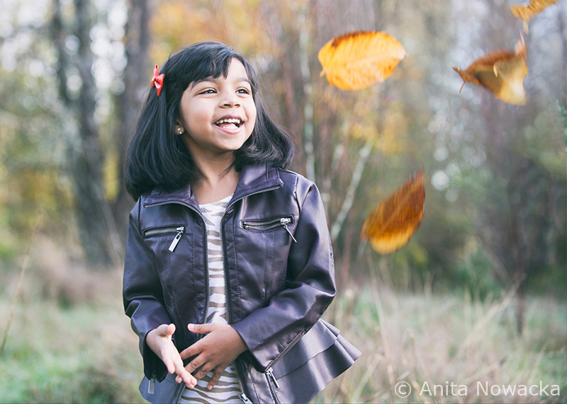 Girl being mesmerized by the leaves being thrown at her by a parent